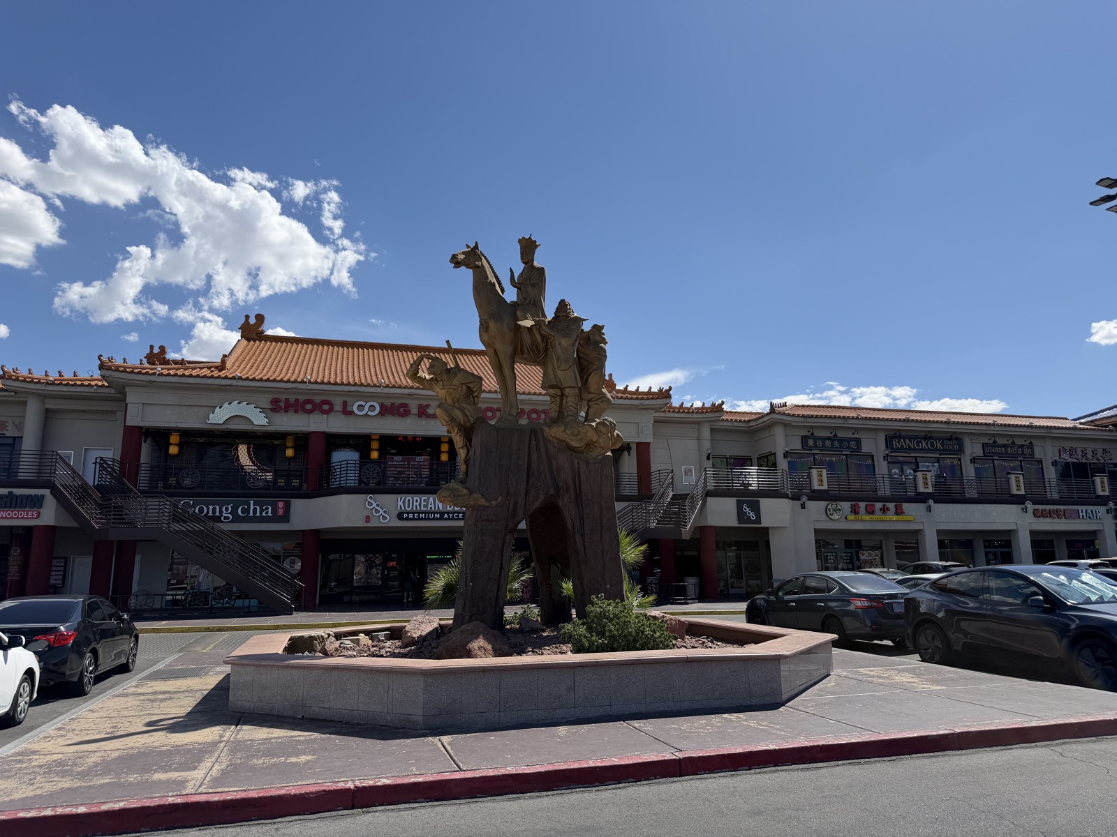 The bronze Journey to the West statue in the courtyard of Chinatown Plaza, with the plaza's tiled roofline and storefronts behind it