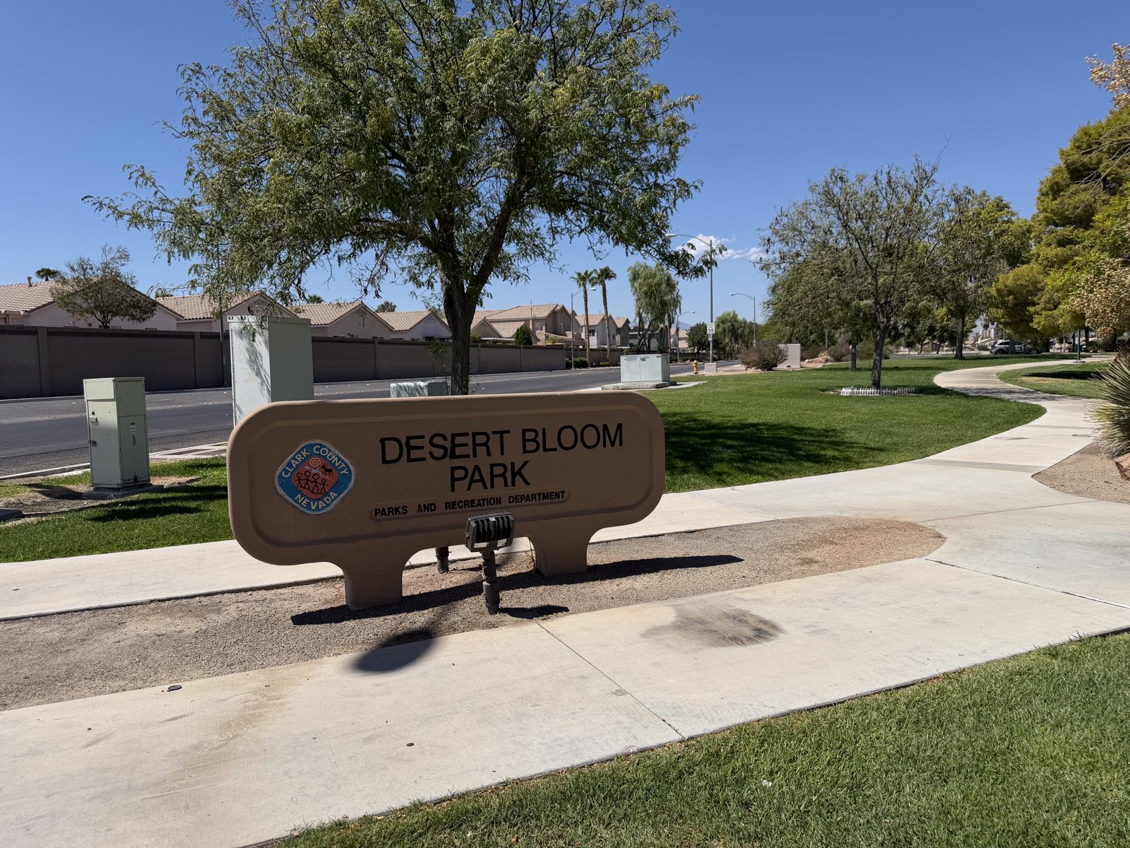 The entrance sign for Desert Bloom Park on South Maryland Parkway in Las Vegas, with the tile-roofed homes and block walls of the surrounding Silverado Ranch neighborhood behind it