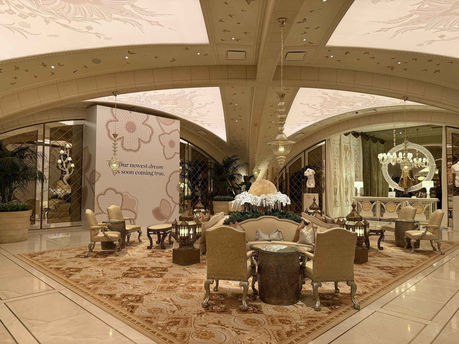 A wide view of the reception lounge at The Spa at Encore Las Vegas, with its illuminated vaulted ceiling, mirrored lattice walls, brass lanterns, and clusters of armchairs around low tables