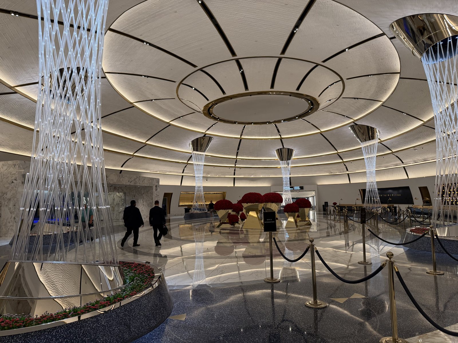 Guests walking through the Fontainebleau Las Vegas arrival rotunda past banks of red roses, under illuminated sculptural columns and a ringed dome