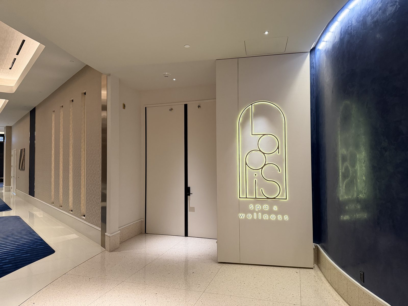 The entrance to Lapis Spa and Wellness at Fontainebleau Las Vegas, with its illuminated wordmark beside a deep blue lacquered wall