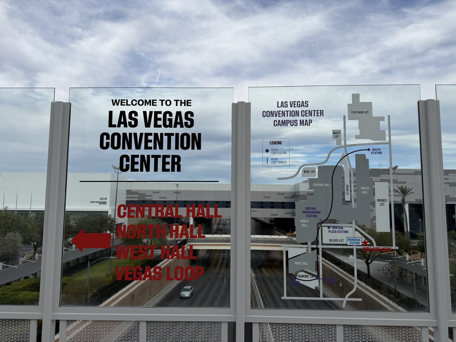 A glass wayfinding panel on the convention center walkway showing the campus map and red lettering directing visitors to the Central Hall, North Hall, West Hall and Vegas Loop