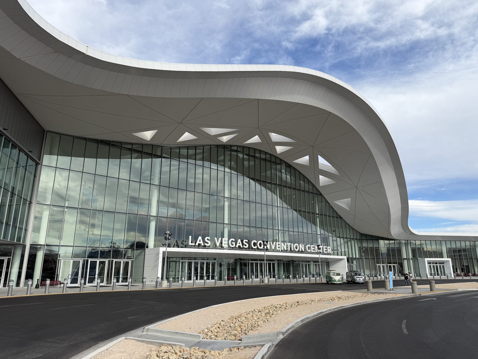 The sweeping white roofline and glass frontage of the Las Vegas Convention Center Central Hall entrance under a blue sky