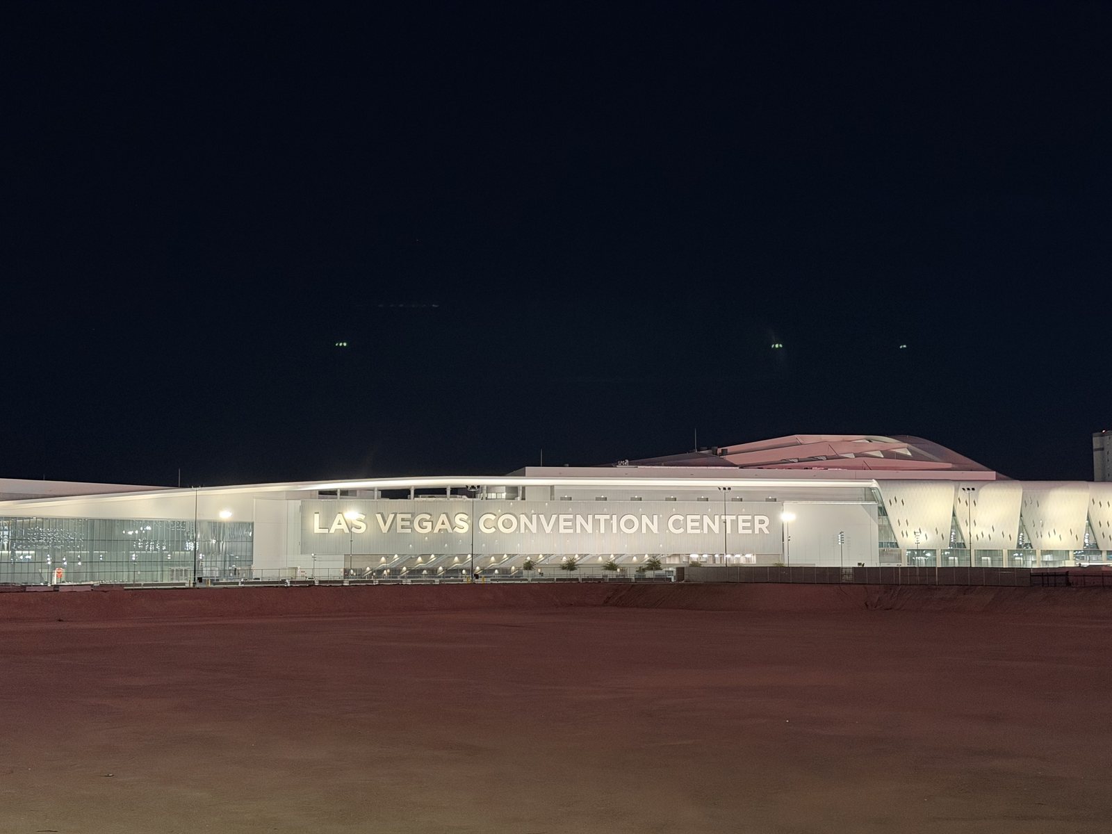 The Las Vegas Convention Center lit up at night, its illuminated name running along the facade above the cleared Riviera site