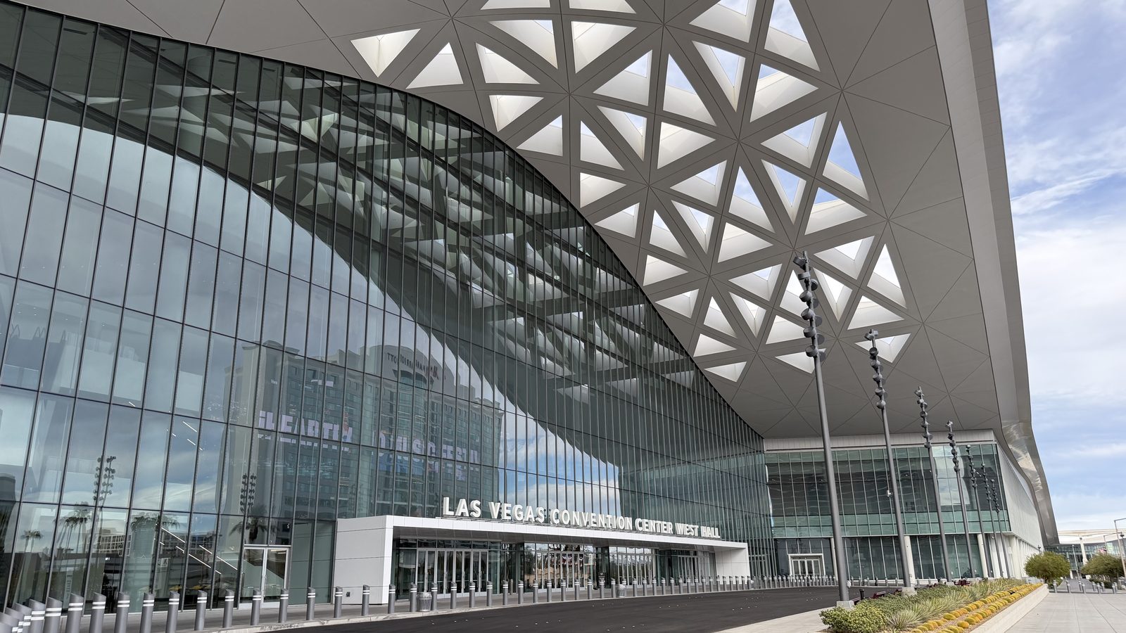 The sweeping perforated white canopy and curved glass facade of the Las Vegas Convention Center West Hall, seen from the entrance drive