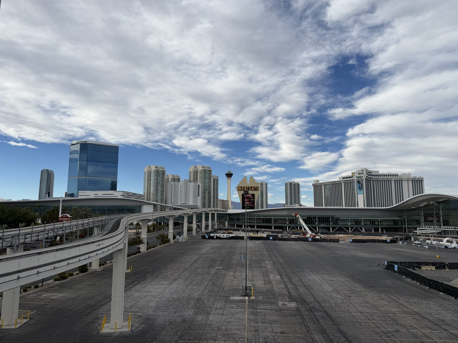 The Las Vegas Monorail guideway curving toward the convention center, with the Fontainebleau tower at left, the Westgate sign, and the Strip skyline in the background under a blue sky