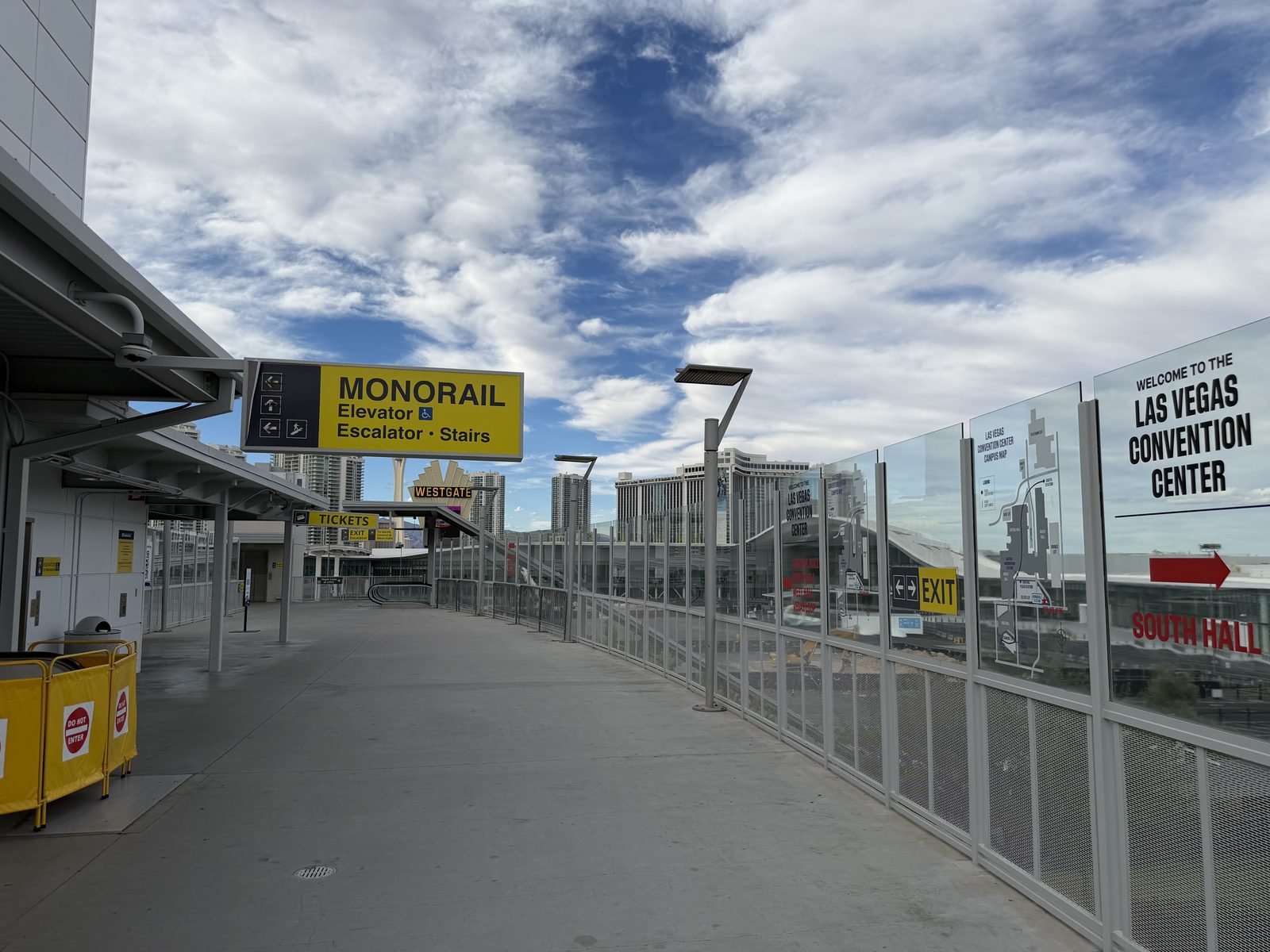 The elevated pedestrian walkway at the Las Vegas Monorail convention center station, with a yellow sign pointing to the elevator, escalator, and stairs and the convention center welcome sign ahead