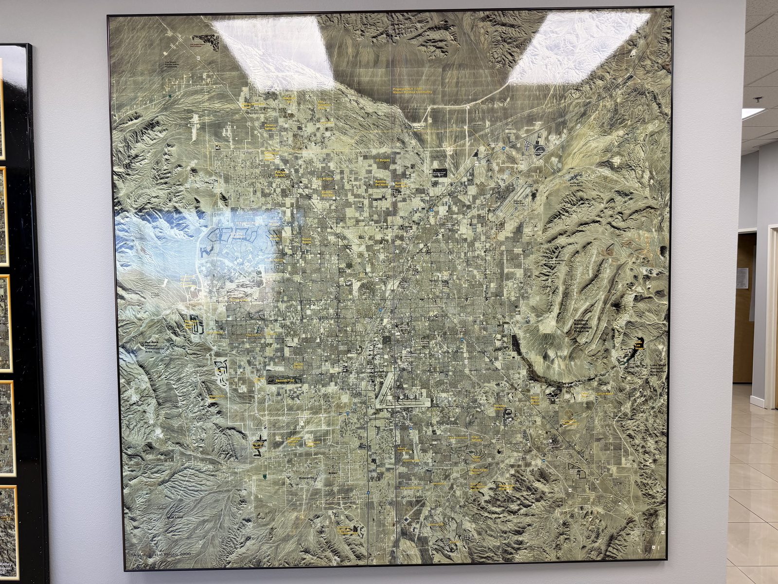 A second relief map of the Las Vegas valley on the office wall, framed to show the mountain ranges closing in around the developed floor
