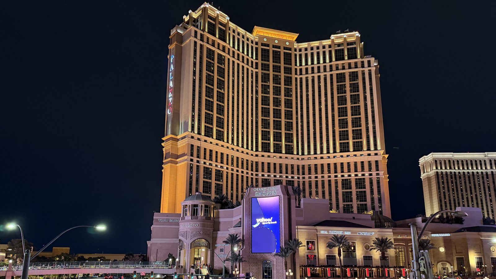 The Palazzo tower lit gold at dusk above the Las Vegas Strip, with traffic on Las Vegas Boulevard in the foreground