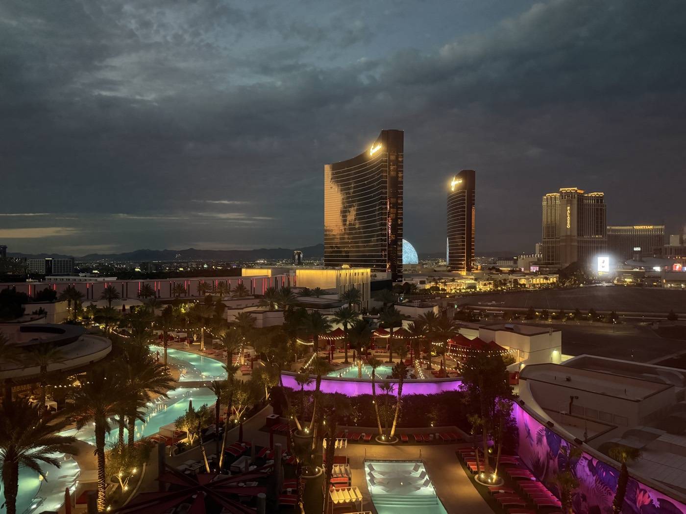 The Resorts World pool complex lit up at night, with the Wynn and Encore towers beyond