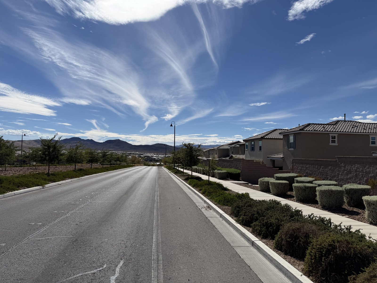 A master-planned residential street in the Las Vegas valley, with tile-roofed homes along one side and the mountains on the horizon
