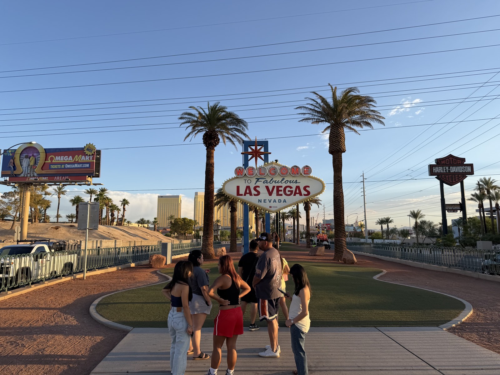 Visitors at the Welcome to Fabulous Las Vegas sign at golden hour, with the Strip skyline in the distance